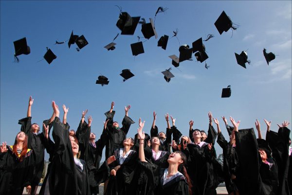 Group of people wearing graduation gear and throwing graduation hats in the air